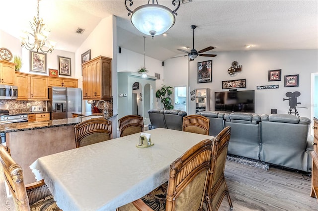dining space with ceiling fan, wood finished floors, high vaulted ceiling, a chandelier, and a textured ceiling