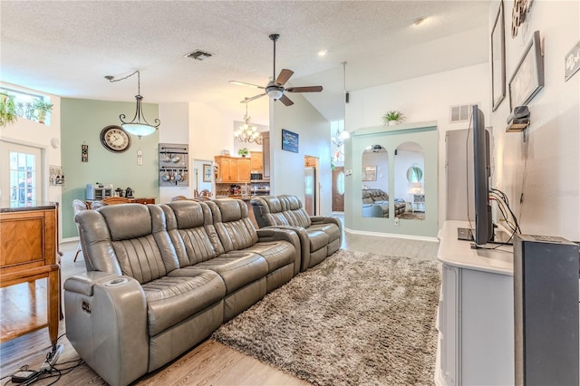 living room with light wood finished floors, ceiling fan, vaulted ceiling, a textured ceiling, and a chandelier