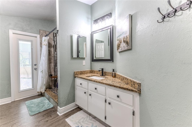 bathroom with wood finished floors, a shower stall, vanity, and a textured wall