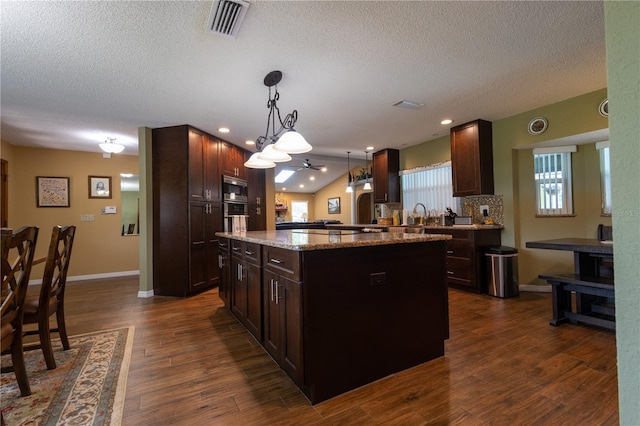 7550 Jomel Dr, Weeki Wachee, FL 34607 - kitchen with a textured ceiling, a kitchen island, dark brown cabinets, light stone countertops, and pendant lighting
