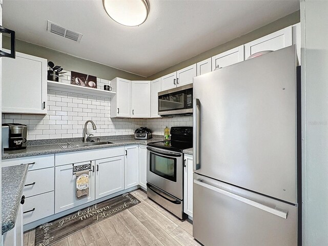 11722 Carissa Ln Unit 49A, New Port Richey, FL 34654 - kitchen with appliances with stainless steel finishes, open shelves, white cabinetry, decorative backsplash, and light wood-style floors