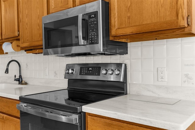 14645 Spellman Ct, Spring Hill, FL 34610 - kitchen with stainless steel appliances, light countertops, brown cabinetry, and backsplash