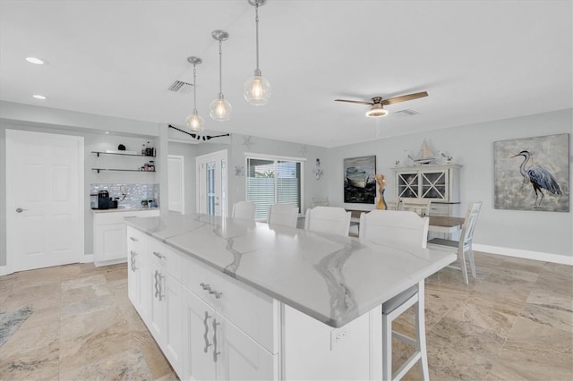 3701 Corsair Ct, New Port Richey, FL 34652 - kitchen with white cabinets, a center island, light stone counters, a breakfast bar area, and hanging light fixtures