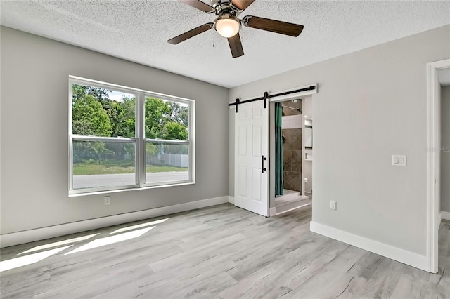 4360 Talco Ave, Spring Hill, FL 34609 - unfurnished bedroom featuring a textured ceiling, light wood-style floors, a barn door, ceiling fan, and ensuite bathroom