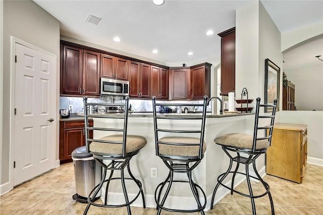 11101 Ragsdale Ct, New Port Richey, FL 34654 - kitchen with stainless steel microwave, arched walkways, a breakfast bar, a peninsula, and recessed lighting