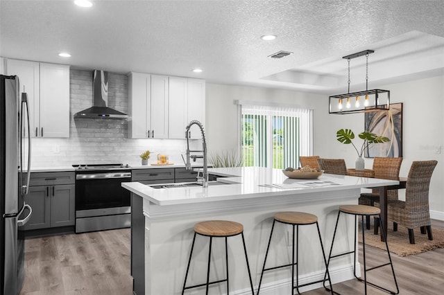 5555 Baffin Cir, Spring Hill, FL 34606 - kitchen featuring stainless steel appliances, wall chimney range hood, light wood finished floors, a textured ceiling, and a kitchen bar