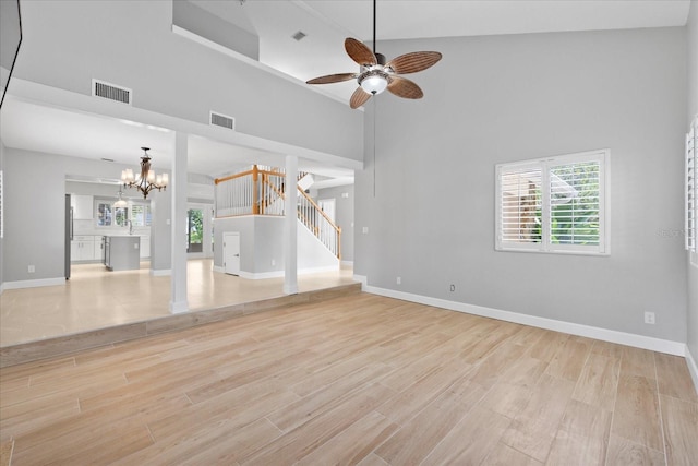 4439 Reeves Rd, New Port Richey, FL 34652 - unfurnished living room featuring ceiling fan, a chandelier, light wood finished floors, a high ceiling, and stairs