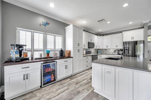 9309 Edistro Pl, New Port Richey, FL 34654 - kitchen featuring appliances with stainless steel finishes, beverage cooler, dark countertops, tasteful backsplash, and light wood finished floors