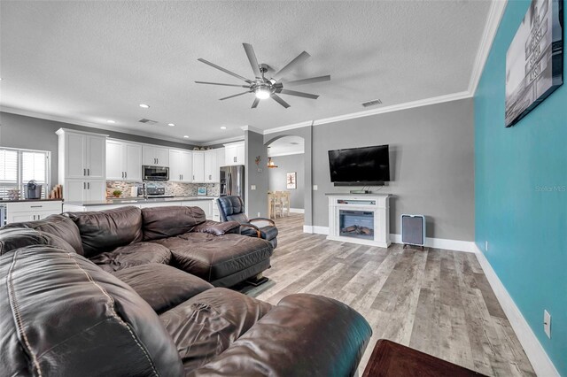 9309 Edistro Pl, New Port Richey, FL 34654 - living room with ceiling fan, a textured ceiling, light wood-style floors, ornamental molding, and arched walkways