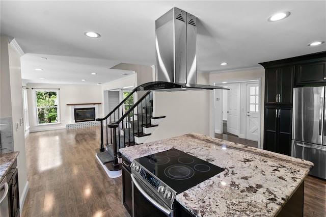 2202 Amity Ct, New Port Richey, FL 34655 - kitchen with appliances with stainless steel finishes, island exhaust hood, light stone counters, dark wood-style flooring, and a glass covered fireplace