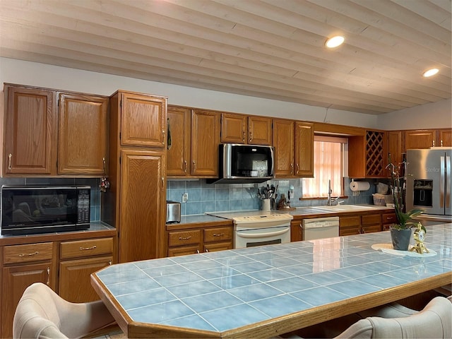 20971 Negril Ct, Lutz, FL 33558 - kitchen with tile counters, white appliances, vaulted ceiling, brown cabinetry, and backsplash