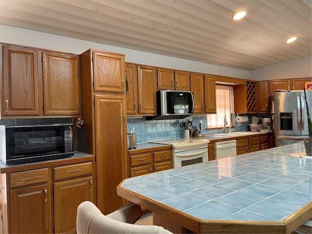20971 Negril Ct, Lutz, FL 33558 - kitchen with appliances with stainless steel finishes, tile counters, brown cabinetry, vaulted ceiling, and recessed lighting
