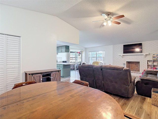 9425 Sterling Ln, Port Richey, FL 34668 - dining room featuring light wood-style flooring, a ceiling fan, vaulted ceiling, a textured ceiling, and a fireplace