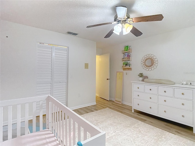 9425 Sterling Ln, Port Richey, FL 34668 - bedroom featuring light wood-style flooring, a textured ceiling, a crib, a closet, and a ceiling fan