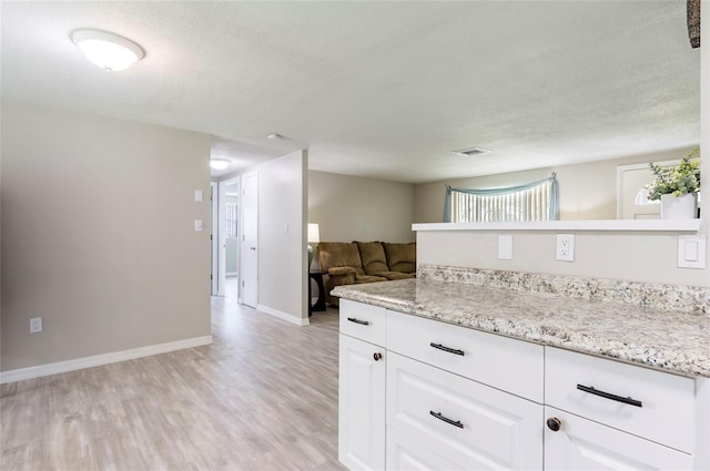 10600 Oleander Dr, Port Richey, FL 34668 - kitchen with light wood-style floors, white cabinetry, a textured ceiling, open floor plan, and light stone counters