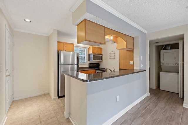 2500 Winding Creek Blvd Unit G106, Clearwater, FL 33761 - kitchen with appliances with stainless steel finishes, stacked washer and clothes dryer, dark countertops, a peninsula, and crown molding