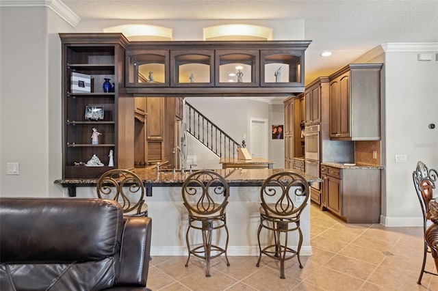 26221 Pheasant Run, Wesley Chapel, FL 33544 - kitchen featuring a breakfast bar, dark stone countertops, glass insert cabinets, a peninsula, and crown molding