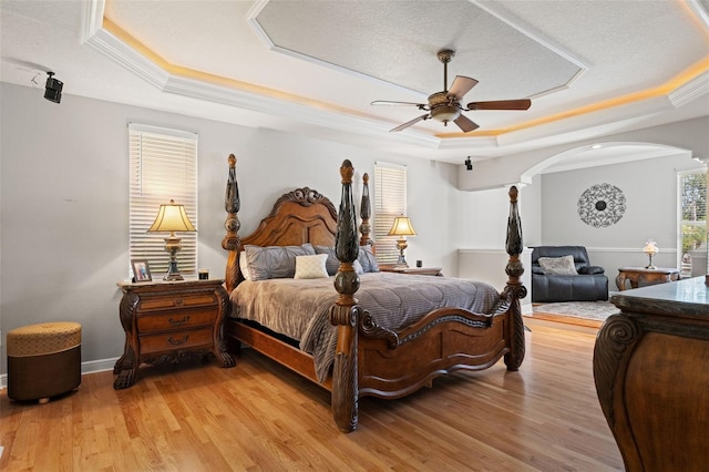 26221 Pheasant Run, Wesley Chapel, FL 33544 - bedroom featuring a tray ceiling, arched walkways, light wood finished floors, a ceiling fan, and crown molding