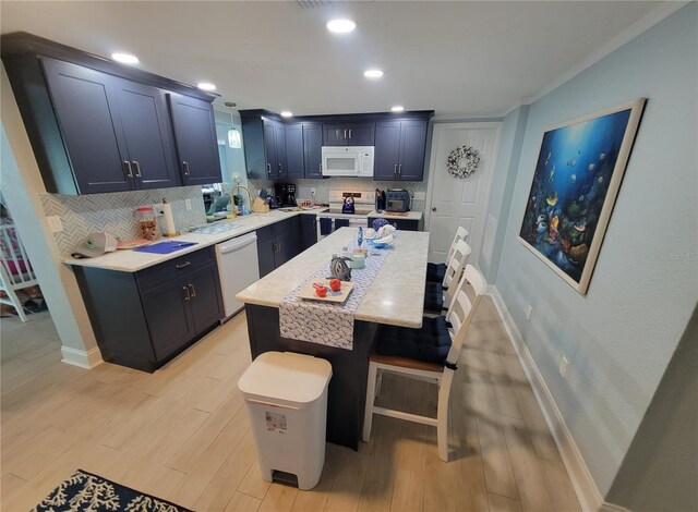 6737 Clark St, Hudson, FL 34667 - kitchen with white appliances, decorative backsplash, light wood-type flooring, a kitchen bar, and a center island