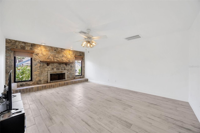 8143 Channel Dr, Port Richey, FL 34668 - unfurnished living room featuring light wood-style floors, healthy amount of natural light, ceiling fan, and a stone fireplace