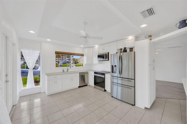 8143 Channel Dr, Port Richey, FL 34668 - kitchen with stainless steel appliances, white cabinetry, ceiling fan, a raised ceiling, and recessed lighting
