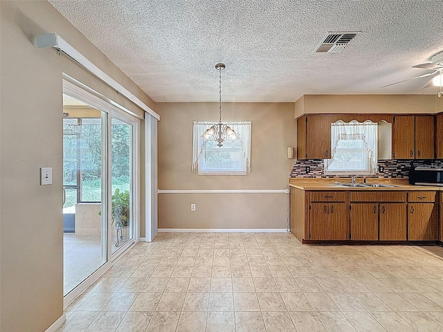 11094 Auburndale St, Spring Hill, FL 34609 - kitchen with brown cabinets, backsplash, plenty of natural light, a textured ceiling, and a chandelier