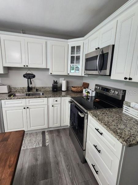 5710 Broadway Ave, New Port Richey, FL 34652 - kitchen featuring appliances with stainless steel finishes, white cabinetry, dark wood-type flooring, and dark stone countertops