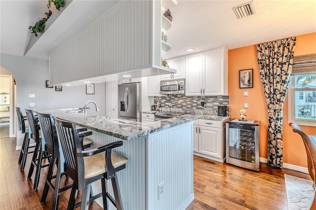 3431 Croaker Dr, Hernando Beach, FL 34607 - kitchen with appliances with stainless steel finishes, beverage cooler, light wood finished floors, and white cabinetry