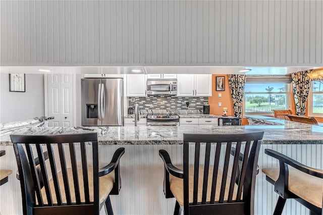 3431 Croaker Dr, Hernando Beach, FL 34607 - kitchen featuring appliances with stainless steel finishes, white cabinets, a breakfast bar area, backsplash, and light stone counters