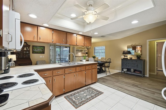 18531 Ozark Dr, Hudson, FL 34667 - kitchen featuring tile counters, brown cabinets, a tray ceiling, recessed lighting, and light wood-style floors