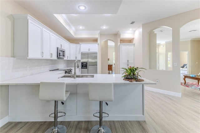 5301 Legend Hills Ln, Spring Hill, FL 34609 - kitchen featuring stainless steel appliances, a peninsula, arched walkways, light wood-style floors, and ornamental molding