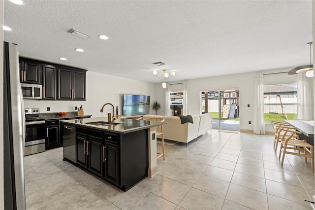 12948 Conquistador Loop, Spring Hill, FL 34610 - kitchen featuring stainless steel appliances, dark cabinetry, open floor plan, a center island with sink, and light tile patterned floors