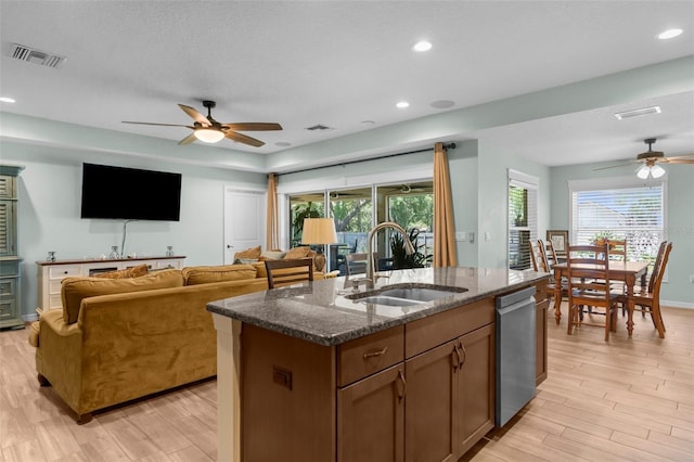 9863 Deer St, Spring Hill, FL 34608 - kitchen featuring ceiling fan, stainless steel dishwasher, light wood-style floors, a center island with sink, and dark stone countertops