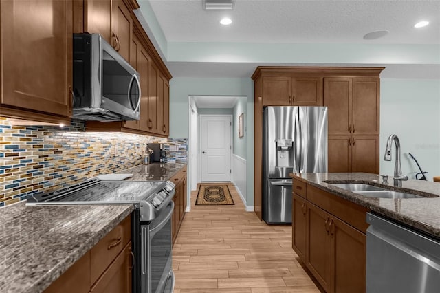 9863 Deer St, Spring Hill, FL 34608 - kitchen with stainless steel appliances, light wood-style flooring, dark stone counters, brown cabinetry, and tasteful backsplash