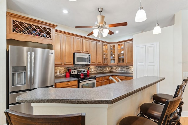 15604 Durango Cir, Brooksville, FL 34604 - kitchen featuring stainless steel appliances, dark countertops, a kitchen bar, decorative backsplash, and a ceiling fan