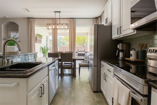 14647 Potterton Cir, Hudson, FL 34667 - kitchen with appliances with stainless steel finishes, dark countertops, backsplash, white cabinets, and pendant lighting
