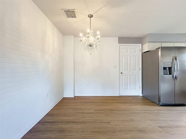 12214 Partridge Hill Row, Hudson, FL 34667 - unfurnished dining area with a chandelier, wood finished floors, brick wall, and a textured ceiling