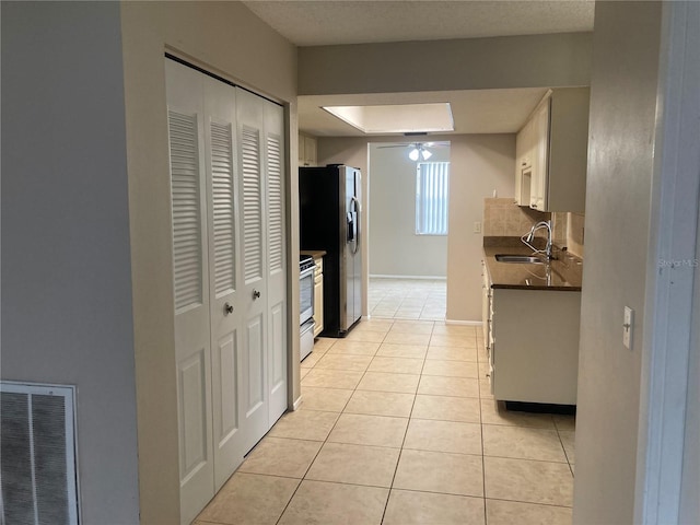 7806 Jenner Ave, New Port Richey, FL 34655 - kitchen featuring dark countertops, stainless steel fridge, range, light tile patterned floors, and a skylight