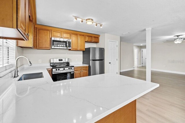4905 Toni Ave, Lakeland, FL 33812 - kitchen featuring appliances with stainless steel finishes, brown cabinetry, a peninsula, light stone countertops, and light wood-style flooring