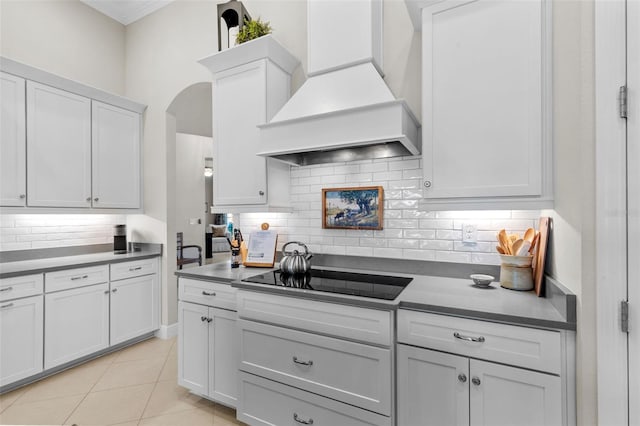 13208 Fawn Lily Dr, Riverview, FL 33579 - kitchen featuring black electric stovetop, custom exhaust hood, tasteful backsplash, arched walkways, and white cabinetry
