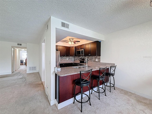 225 Country Club Dr Unit A203, Largo, FL 33771 - kitchen with stainless steel appliances, a textured ceiling, a breakfast bar, a ceiling fan, and decorative backsplash