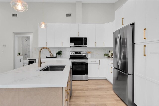 6529 Taylor Ct, New Port Richey, FL 34653 - kitchen featuring stainless steel appliances, tasteful backsplash, light wood-type flooring, a kitchen island with sink, and decorative light fixtures