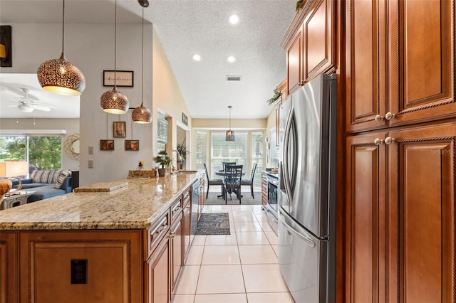 kitchen featuring stainless steel appliances, brown cabinetry, a textured ceiling, light stone countertops, and open floor plan