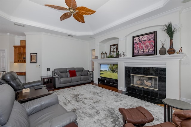 10508 Pontofino Cir, Trinity, FL 34655 - living area with a tray ceiling, a tiled fireplace, ceiling fan, wood finished floors, and ornamental molding