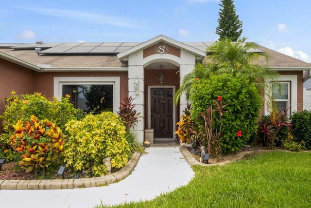 3539 Anniversary Ct, New Port Richey, FL 34653 - view of exterior entry with solar panels, stucco siding, and a shingled roof