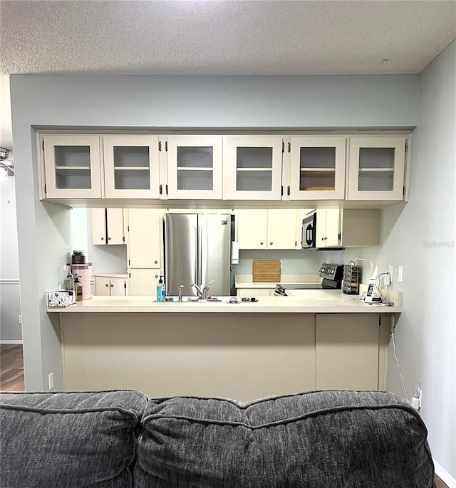 7721 Hillside Ct Unit 203, Hudson, FL 34667 - kitchen featuring appliances with stainless steel finishes, a textured ceiling, a peninsula, glass insert cabinets, and light countertops