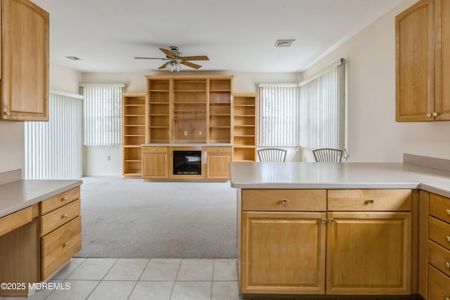 kitchen with light carpet, visible vents, a ceiling fan, light countertops, and a glass covered fireplace