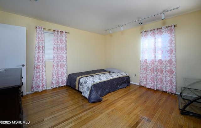 bedroom with multiple windows, hardwood / wood-style floors, and track lighting