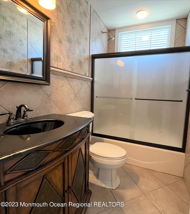 full bathroom featuring tile flooring, shower / bath combination with glass door, tile walls, toilet, and vanity