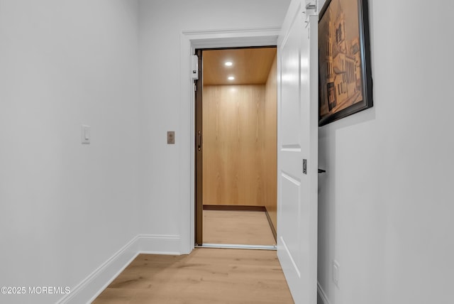 corridor featuring light wood-type flooring, a barn door, and elevator